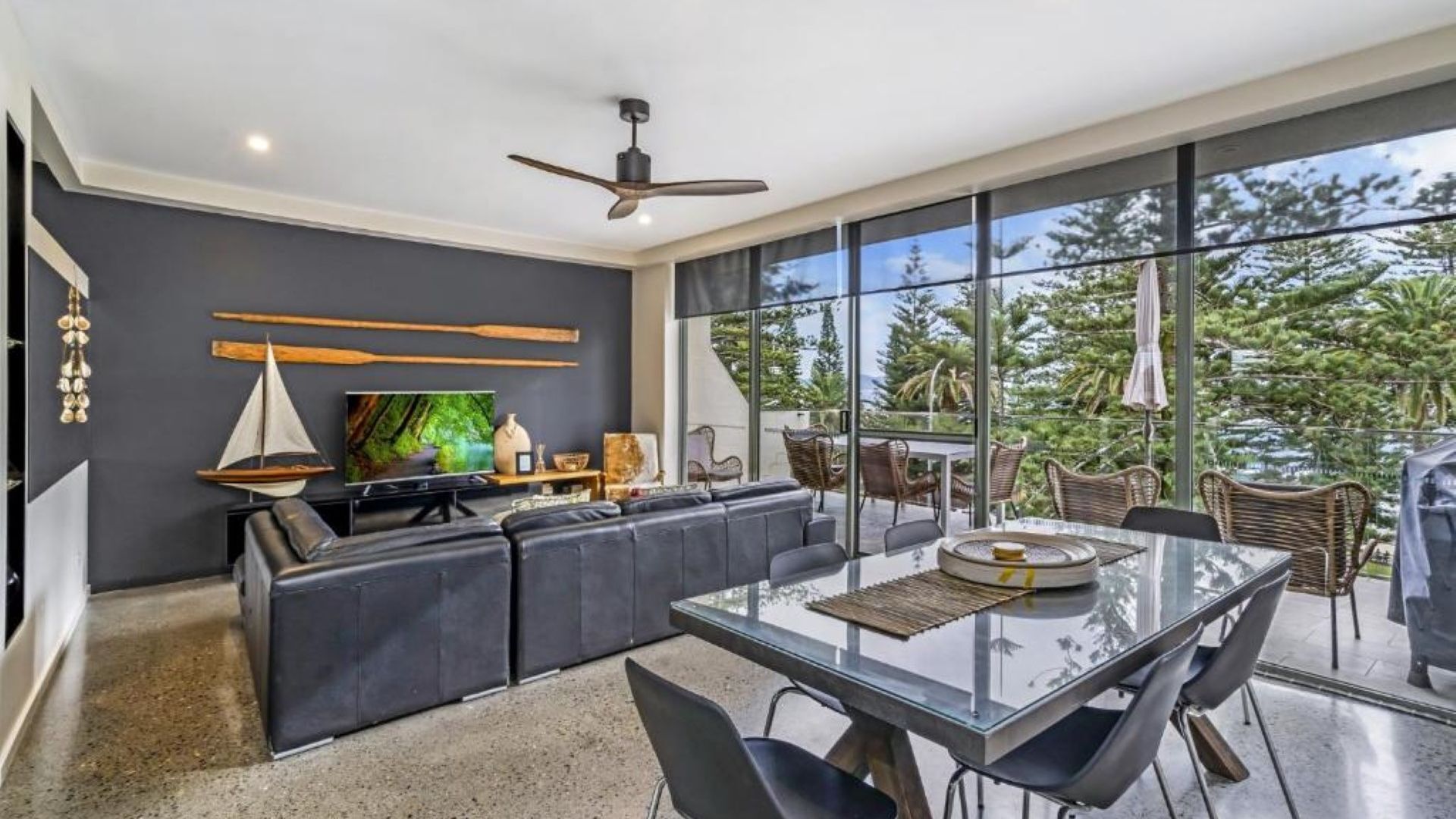A modern living room with a glass dining table, dark sofas, and a television.