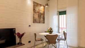 A modern dining area with a round table, four chairs, a vase with flowers, a flat-screen TV on a stand, and a large abstract painting on the wall. - Rome Elements Apartment, elegante, raffinato appartamento a 15 minuti dal centro (Roma)