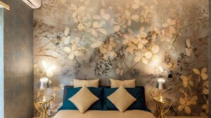 A bedroom with a floral wallpaper, a bed with blue and beige pillows, and two bedside lamps on gold stands. - Rome Elements Apartment, elegante, raffinato appartamento a 15 minuti dal centro (Roma)