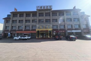A multi-story building with a central entrance, several parked cars, and a clear sky. - Guang'anxin Hotel (Barkol)