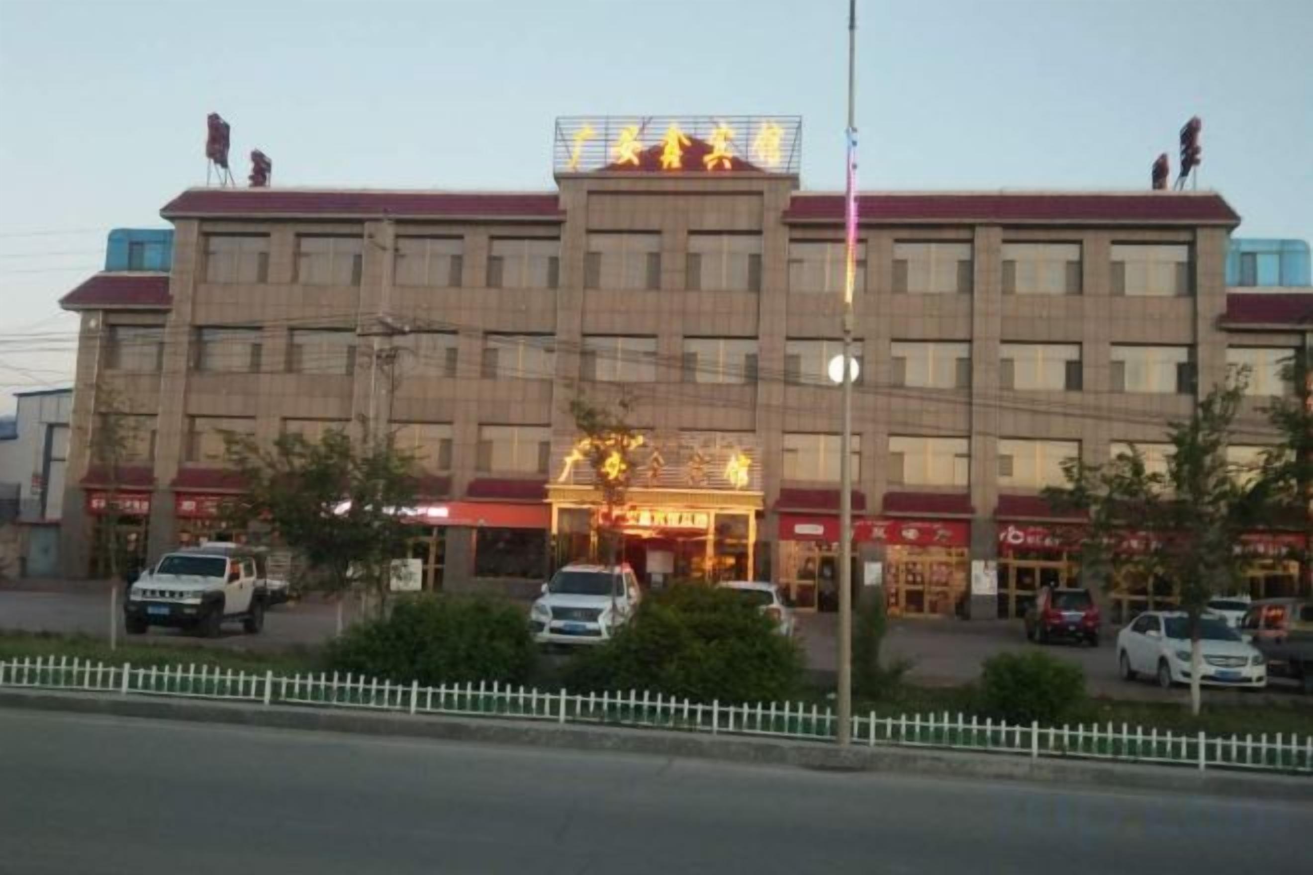 Un hotel de varios pisos con una entrada central, varios espacios de estacionamiento y una cerca blanca en primer plano.