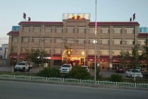 A multi-story hotel with a central entrance, several parking spaces, and a white picket fence in the foreground. - Guang'anxin Hotel (Barkol)