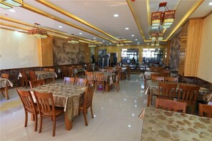 A restaurant with multiple tables and chairs, a tiled floor, and hanging light fixtures. - Guang'anxin Hotel (Barkol)