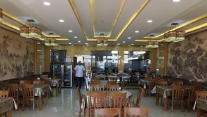 A spacious restaurant with wooden tables and chairs, recessed lighting, and decorative wall murals. - Guang'anxin Hotel (Barkol)