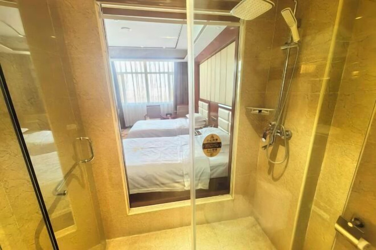 A hotel room with a glass door leading to a shower area, a bed with white linens, and a visible sign with text.