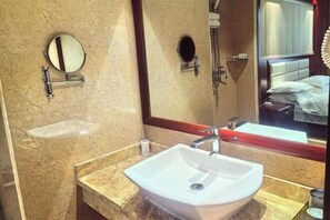 A bathroom with a large mirror, a white sink, and a shower area. - Guang'anxin Hotel (Barkol)