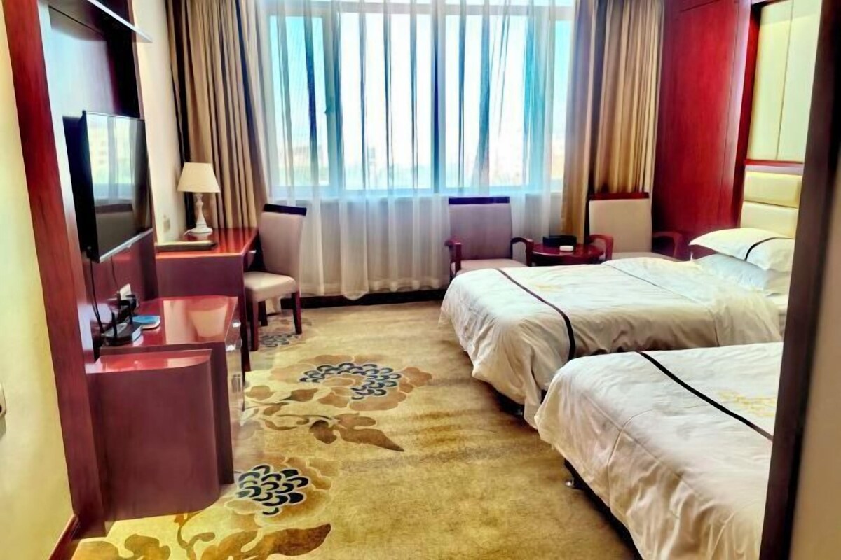 A hotel room with a bed, a desk, a TV, and a window with curtains.