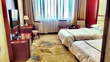 A hotel room with a bed, a desk, a TV, and a window with curtains.