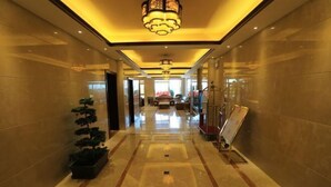 A hotel corridor with a polished marble floor, a potted plant, a reception desk, and a staircase. - Guang'anxin Hotel (Barkol)