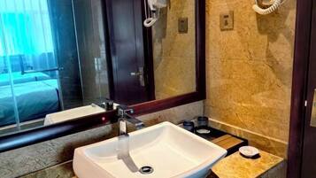 A modern bathroom with a white sink, a mirror, and a hairdryer mounted on the wall.
