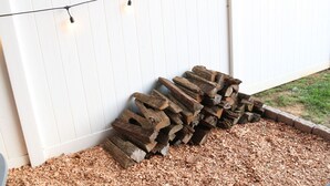 Una cerca de madera blanca con luces encadenadas y una pila de leña.
