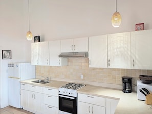 A kitchen with white cabinets, a gas stove, a coffee maker, and pendant lights.