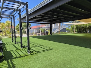 An outdoor gym with a metal frame and artificial turf under a covered area.