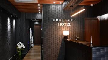 Un área de recepción de hotel con diseño moderno, que incluye un mostrador, un letrero en la pared y un techo de madera.