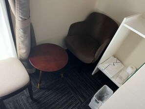 A small room with a round table, a brown chair, a white shelf with toiletries, and a trash bin. - BRILLIANCE HOTEL (Nagoya)