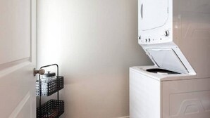Een kleine wasruimte met een witte wasmachine en een metalen droogrek.