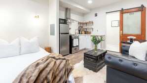 Een compacte hotelkamer met een bed, een slaapbank, een klein tafeltje en een kitchenette met inbouwapparatuur, evenals een badkamer met toilet.