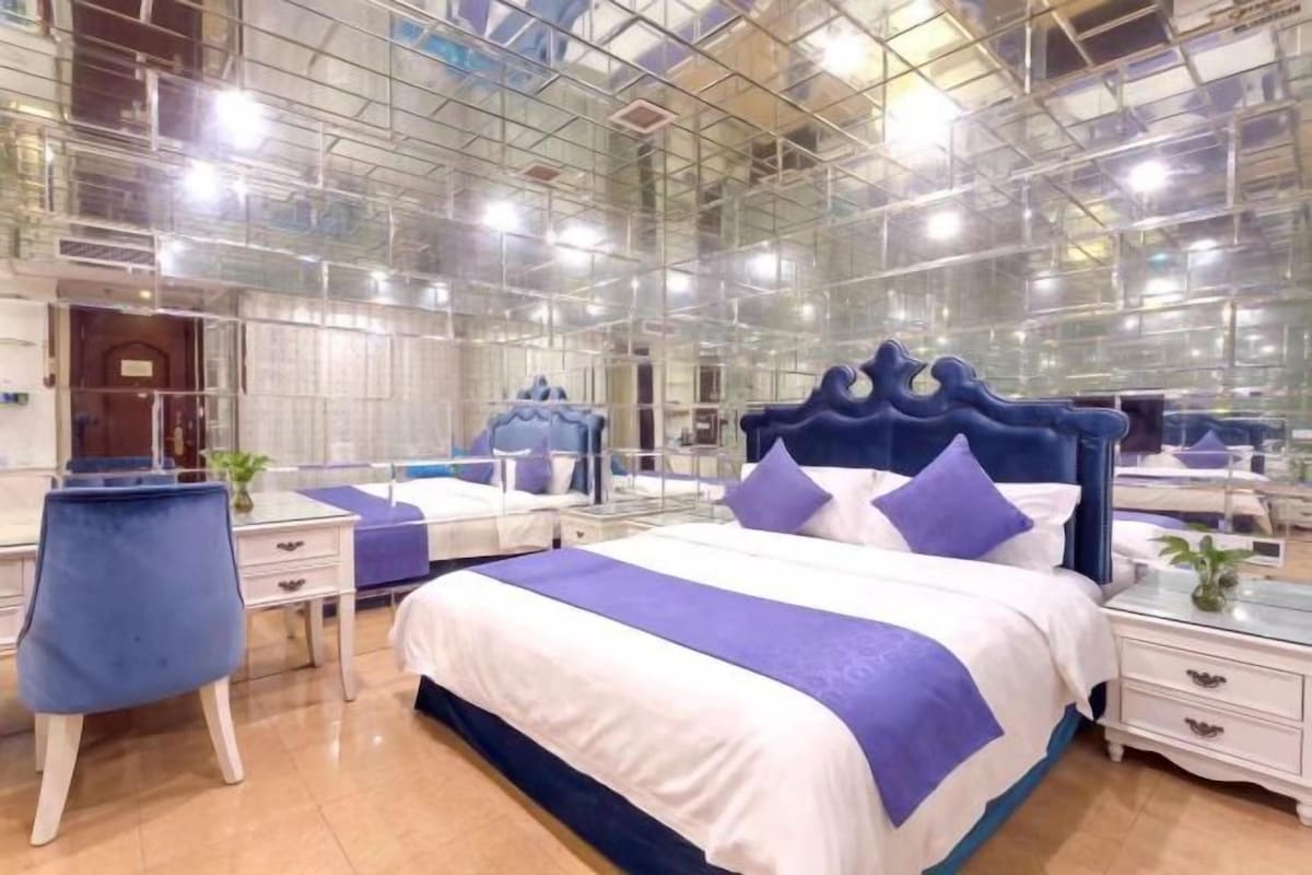 Un dormitorio con un espejo grande, una cama con cabecera azul y un escritorio con una silla.