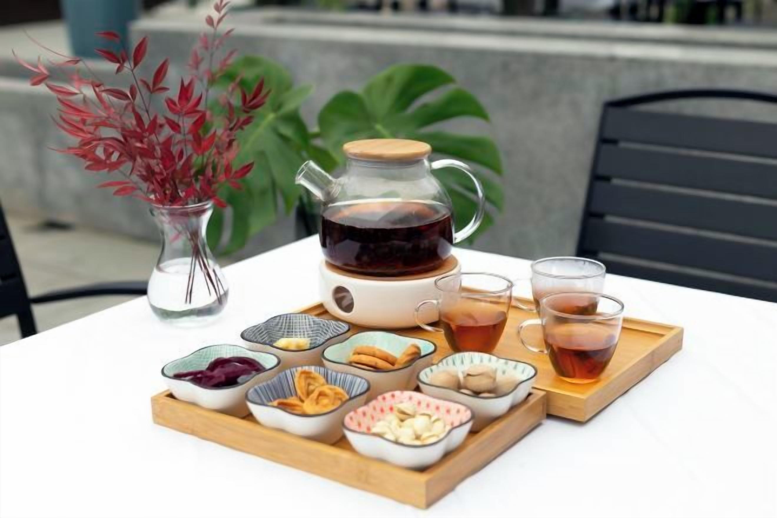 A table with a teapot, cups, and a tray of snacks.