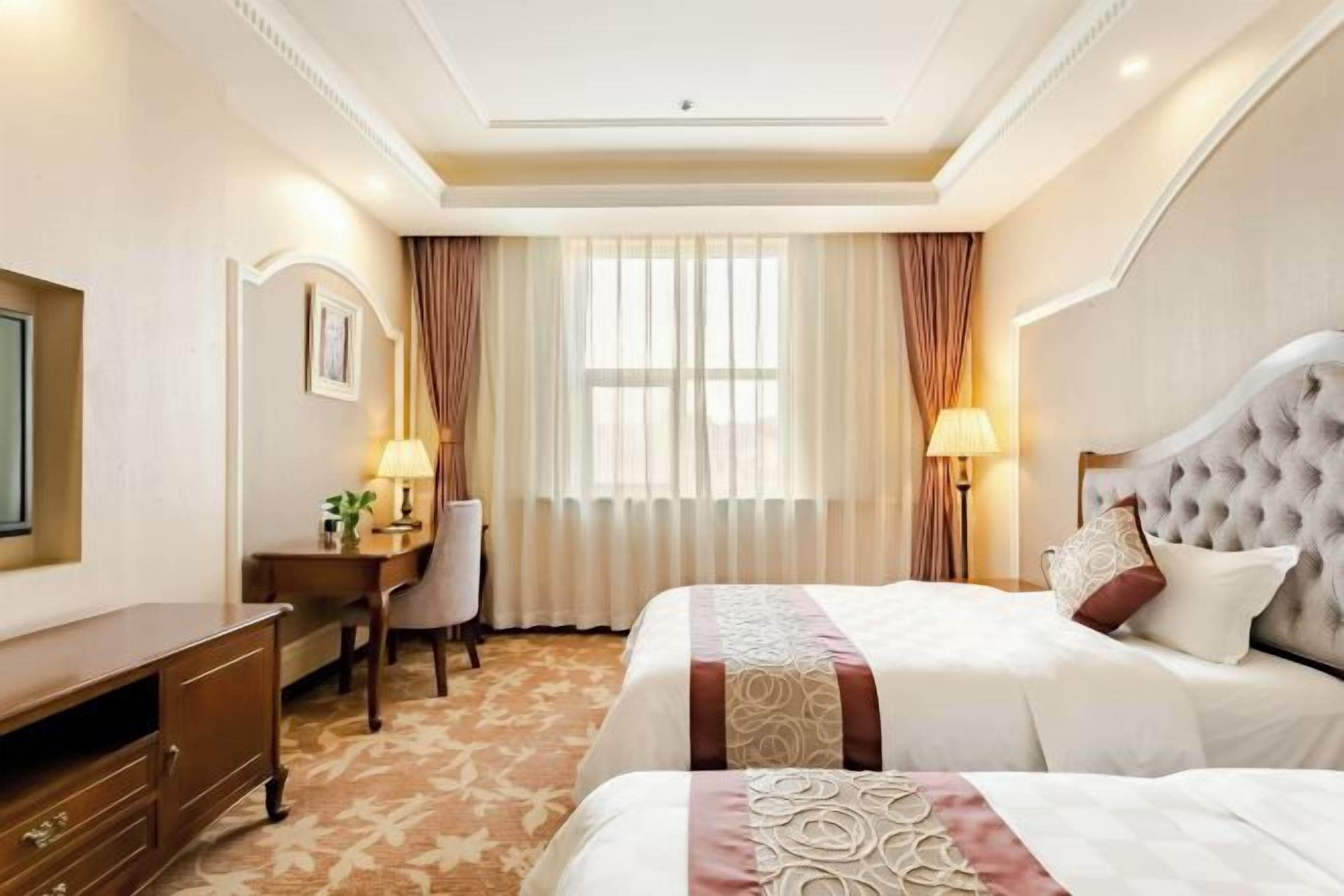 A hotel room with two beds, a desk, a chair, and a television.