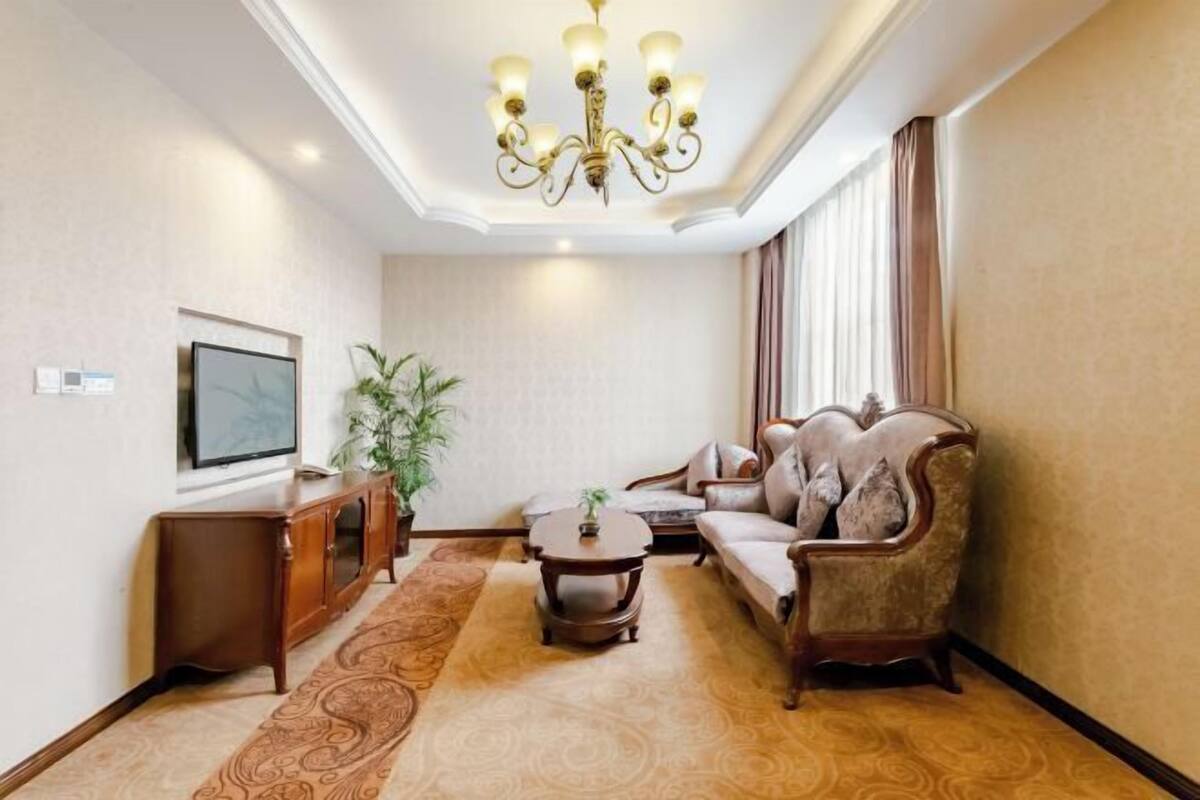 A well-lit living room with a chandelier, a sofa, a coffee table, and a television on a wall.