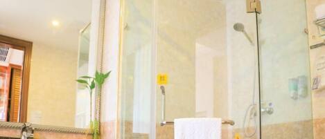 Una ducha con cerramiento de vidrio, una toalla colgada en la puerta, una encimera de mármol y un espejo arriba.