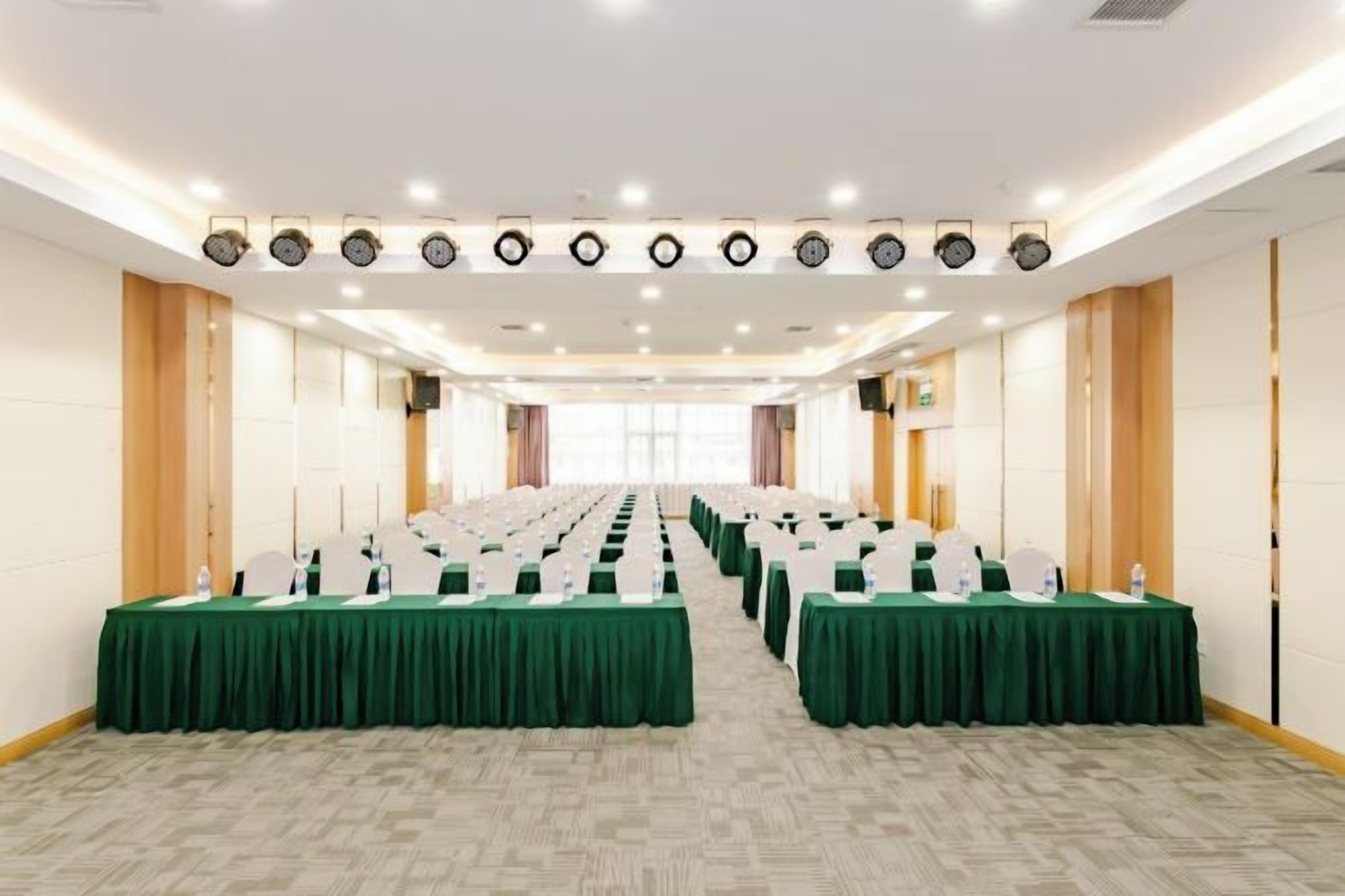 Une salle de conférence avec des rangées de tables, des chaises et une longue table à l’avant.