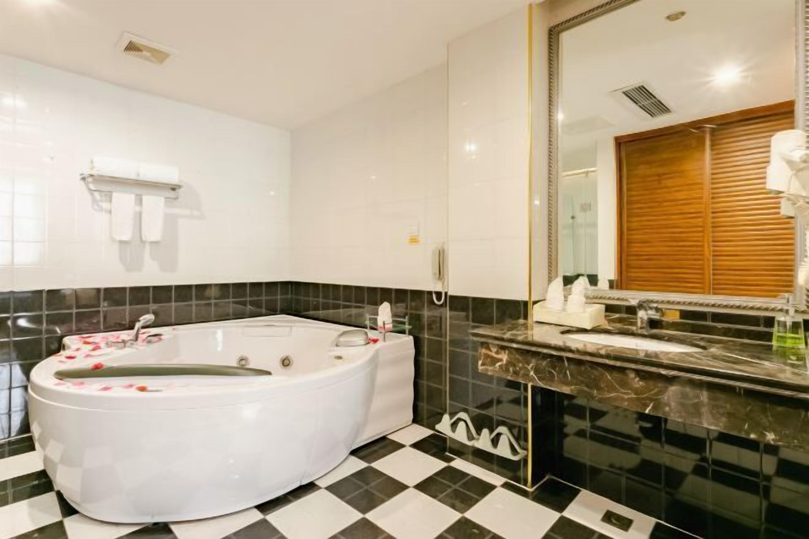 A modern bathroom with a freestanding bathtub, black and white checkered floor, and a large mirror with a wooden panel.