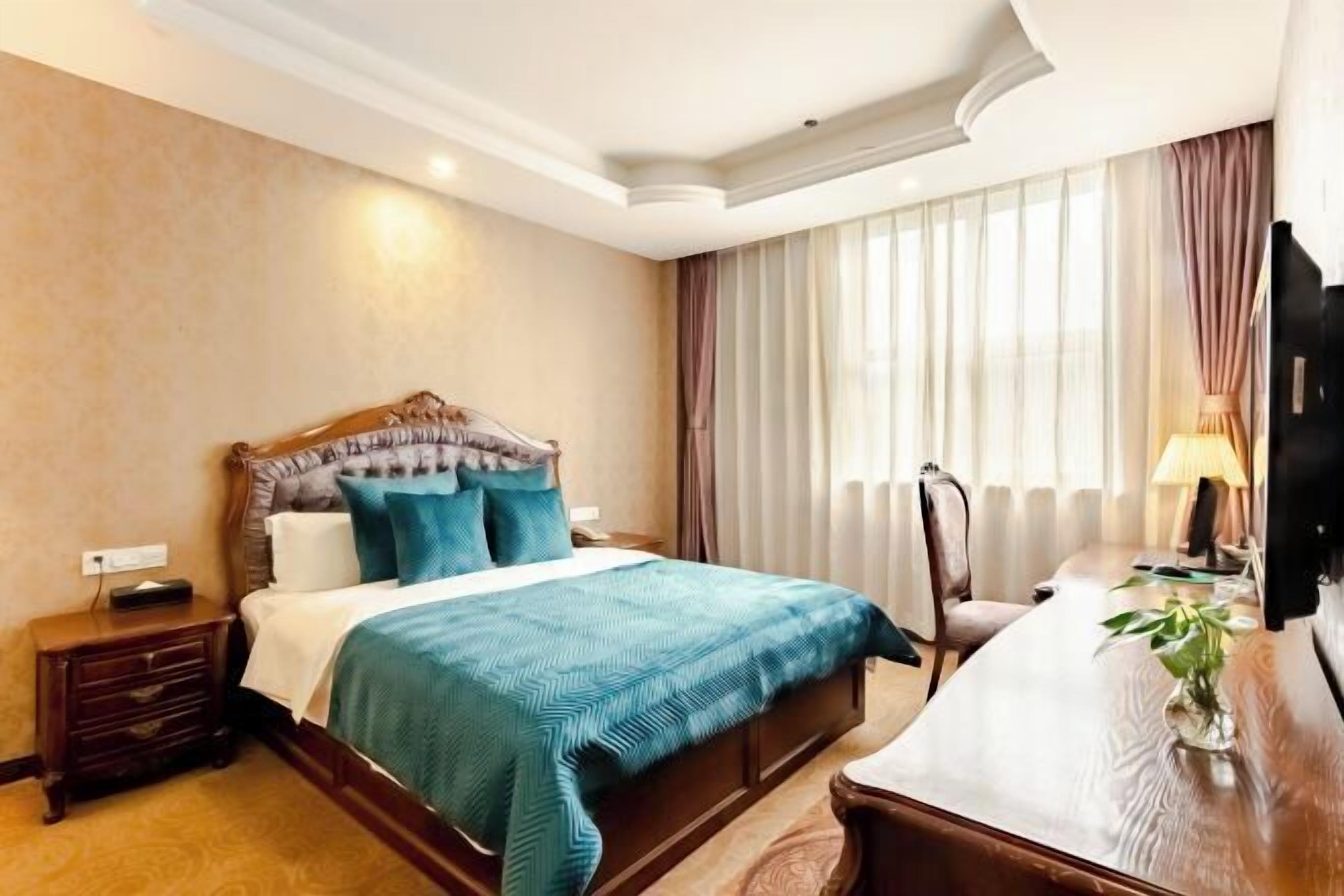Habitación de hotel con una cama grande, un escritorio, una silla, un televisor y una ventana con cortinas.