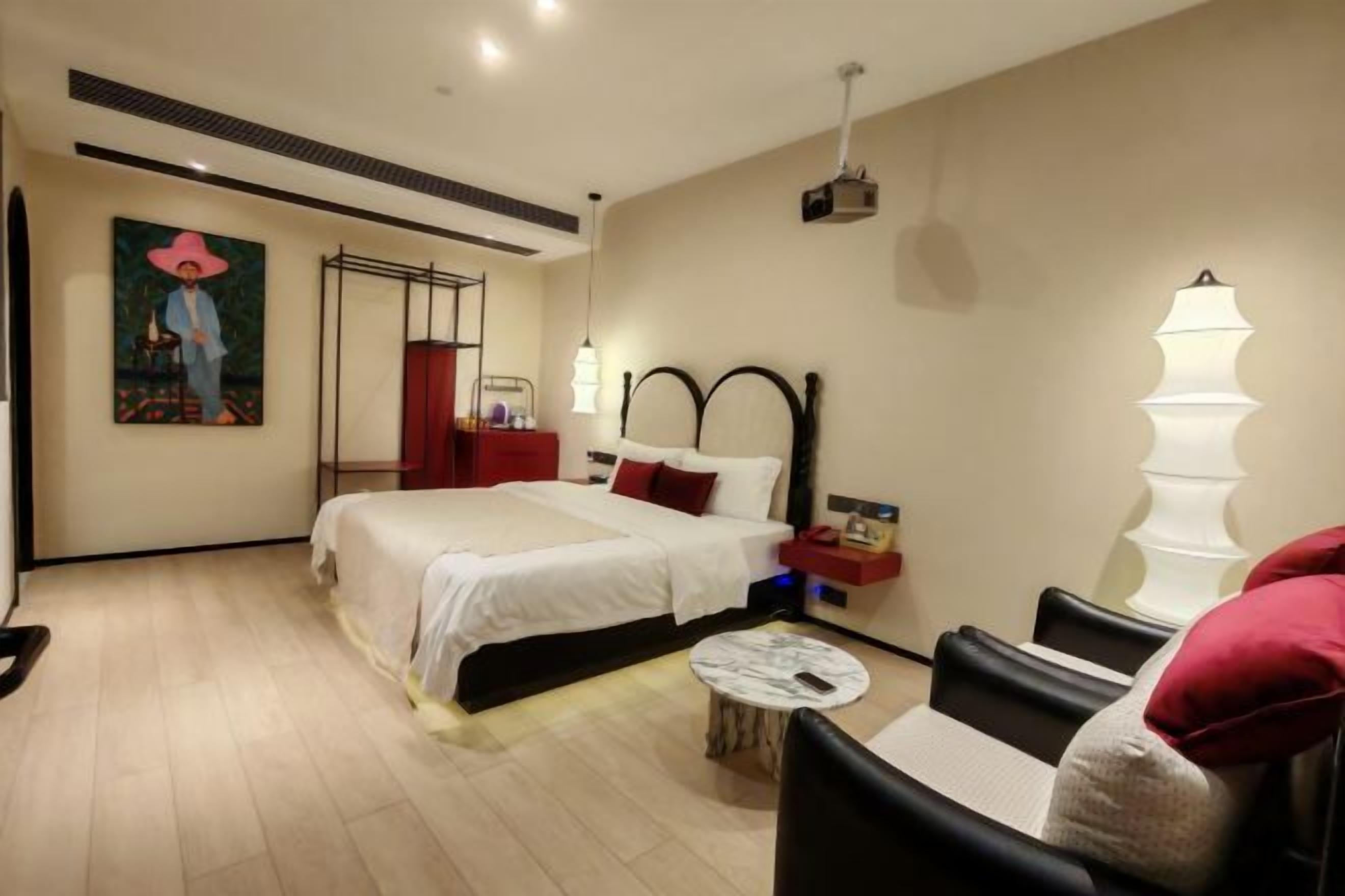 A hotel room with a bed, bedside table, lamp, and a painting on the wall.