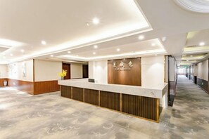 Un hall d’accueil d’hôtel avec un sol en marbre, un comptoir de réception et un couloir menant aux autres chambres.