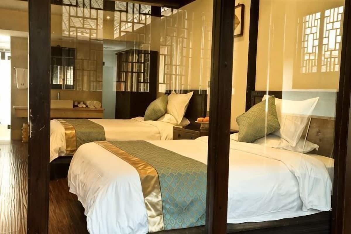 Ein Zimmer mit zwei Betten, Holzboden und einem traditionellen Fenster mit Gittermuster.