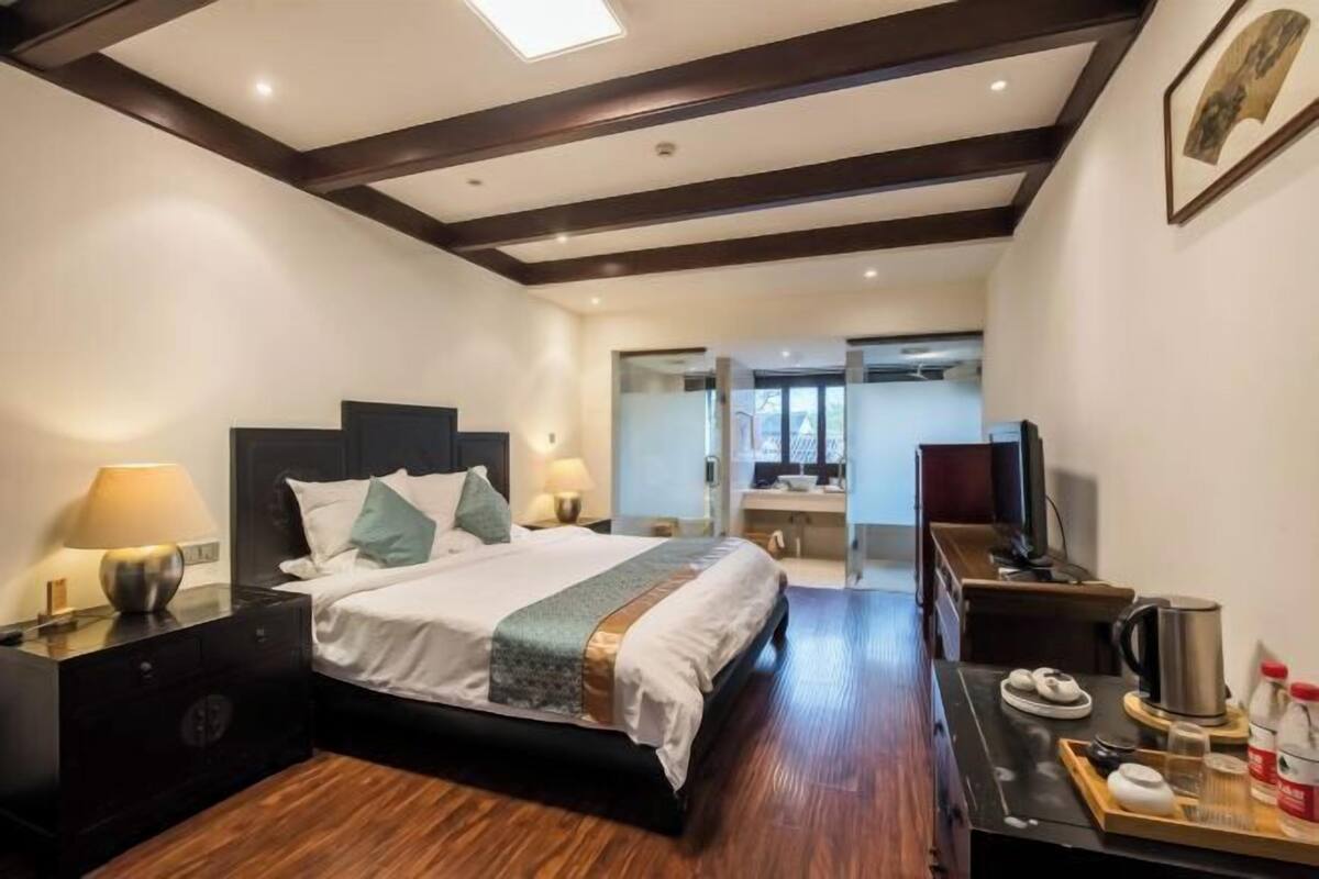 Ein Hotelzimmer mit Bett, Nachttischen, einem Schreibtisch, einem Sessel und einem Fernseher. Ein Badezimmer ist durch eine geöffnete Tür sichtbar.