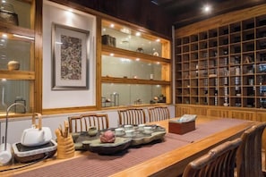 A traditional dining area with a long wooden table, chairs, and a display of pottery. - Yizai Qingyun Chinese-style Courtyard (Kunshan)