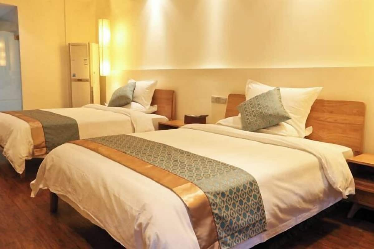 Ein Hotelzimmer mit zwei Betten, Holz-Kopfteilen, Nachttischen und einer Wandleuchte.