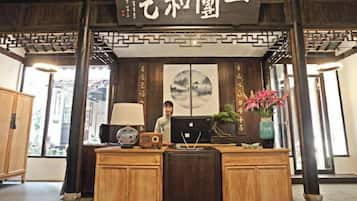 A reception desk with traditional decor, a framed artwork above, and a vase with flowers to the right.
