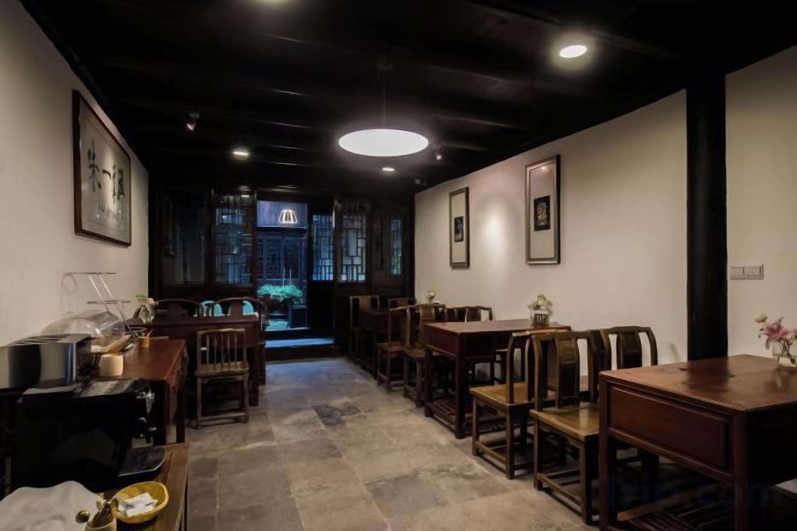 A restaurant interior with wooden tables and chairs, a central walkway, and framed artwork on the walls.