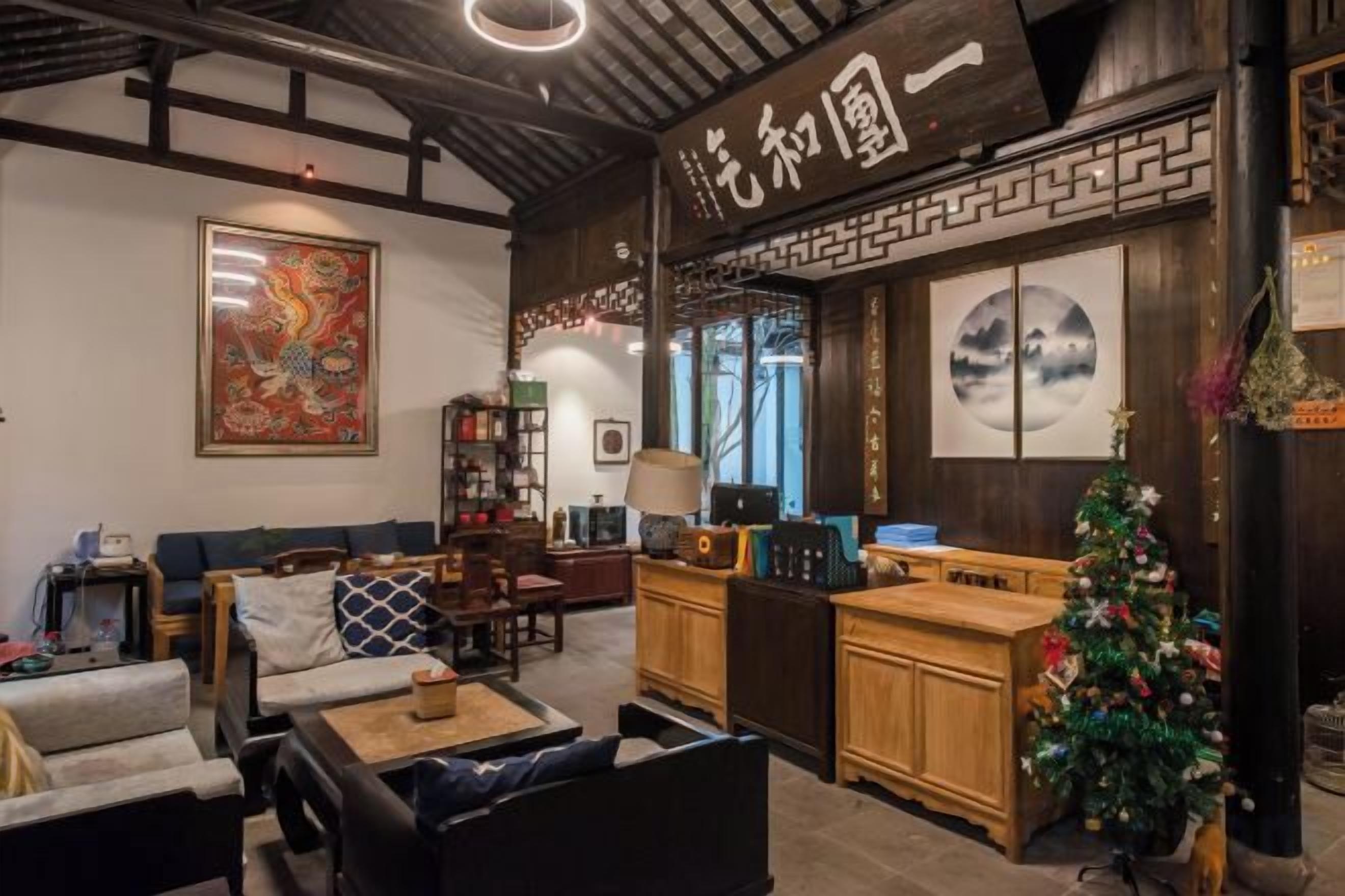 A traditional interior with a wooden reception desk, a Christmas tree, and a large framed artwork on the wall.
