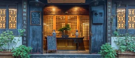 A traditional building with a wooden facade, a signboard, and a small altar with plants.