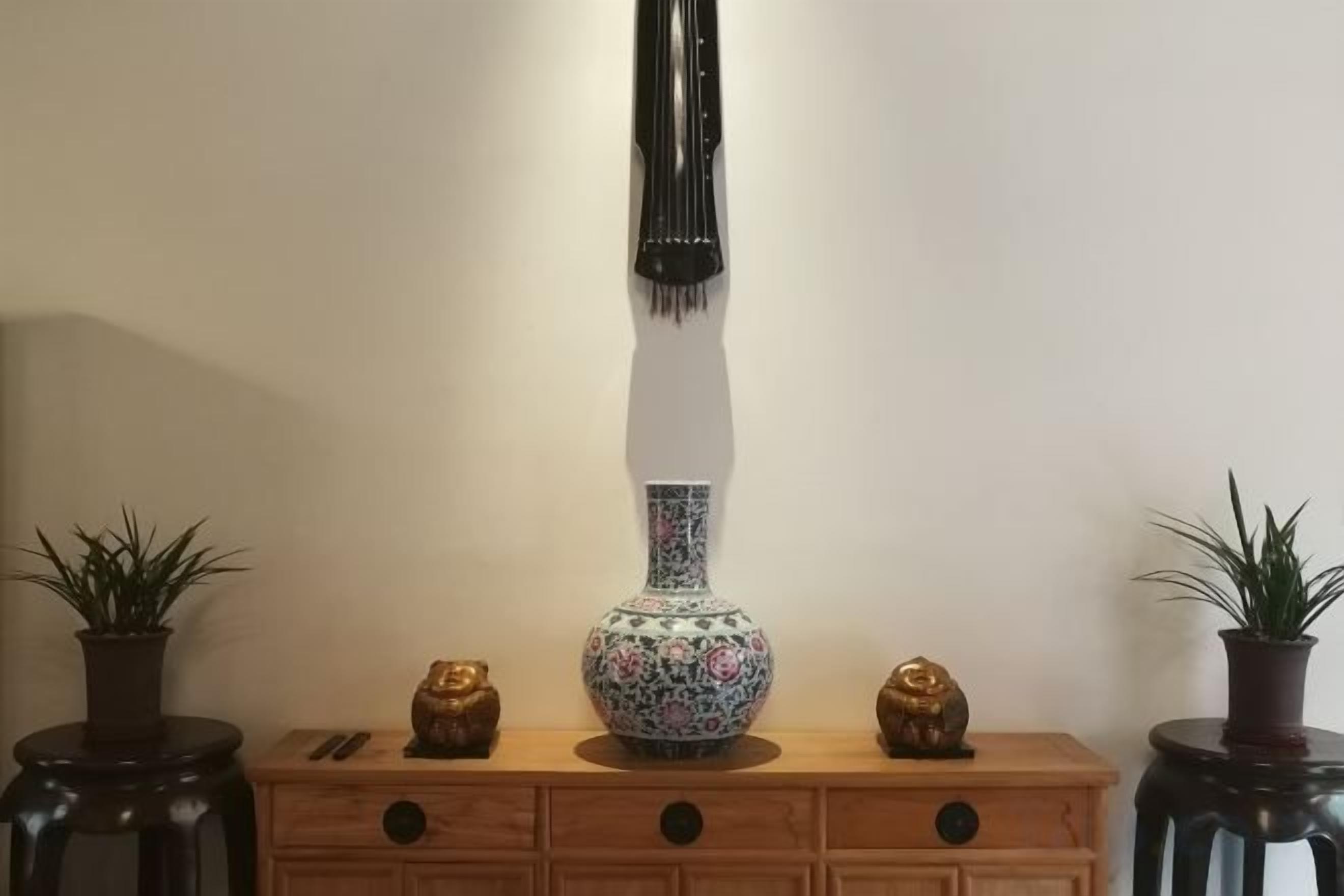 A wooden dresser with a vase, two small golden figurines, and two potted plants.