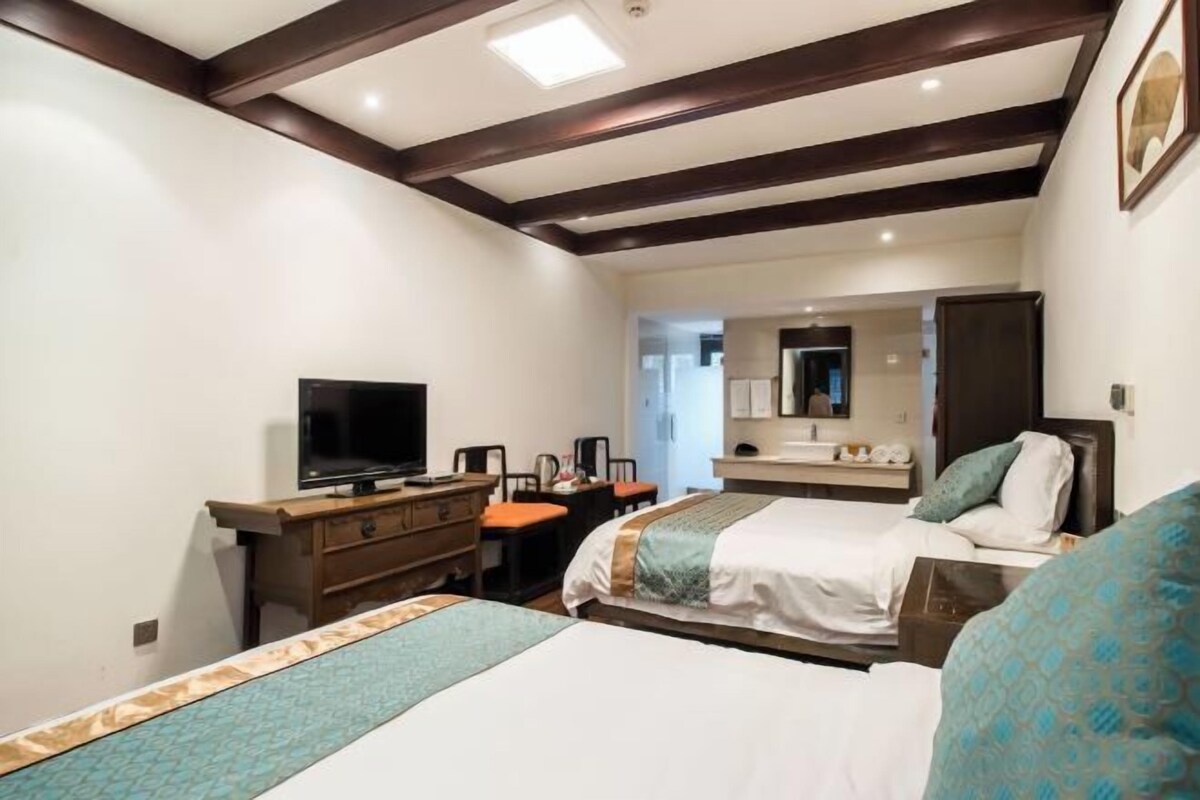 Quarto de hotel com duas camas, uma escrivaninha com televisão, um espelho e um banheiro visível através de uma porta aberta.