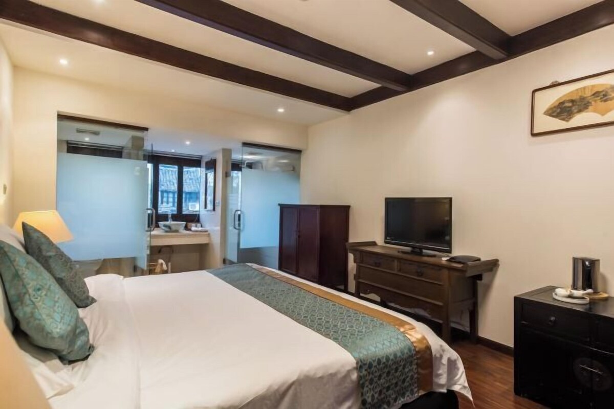 Quarto de hotel com cama, televisão, cômoda e escrivaninha com abajur.