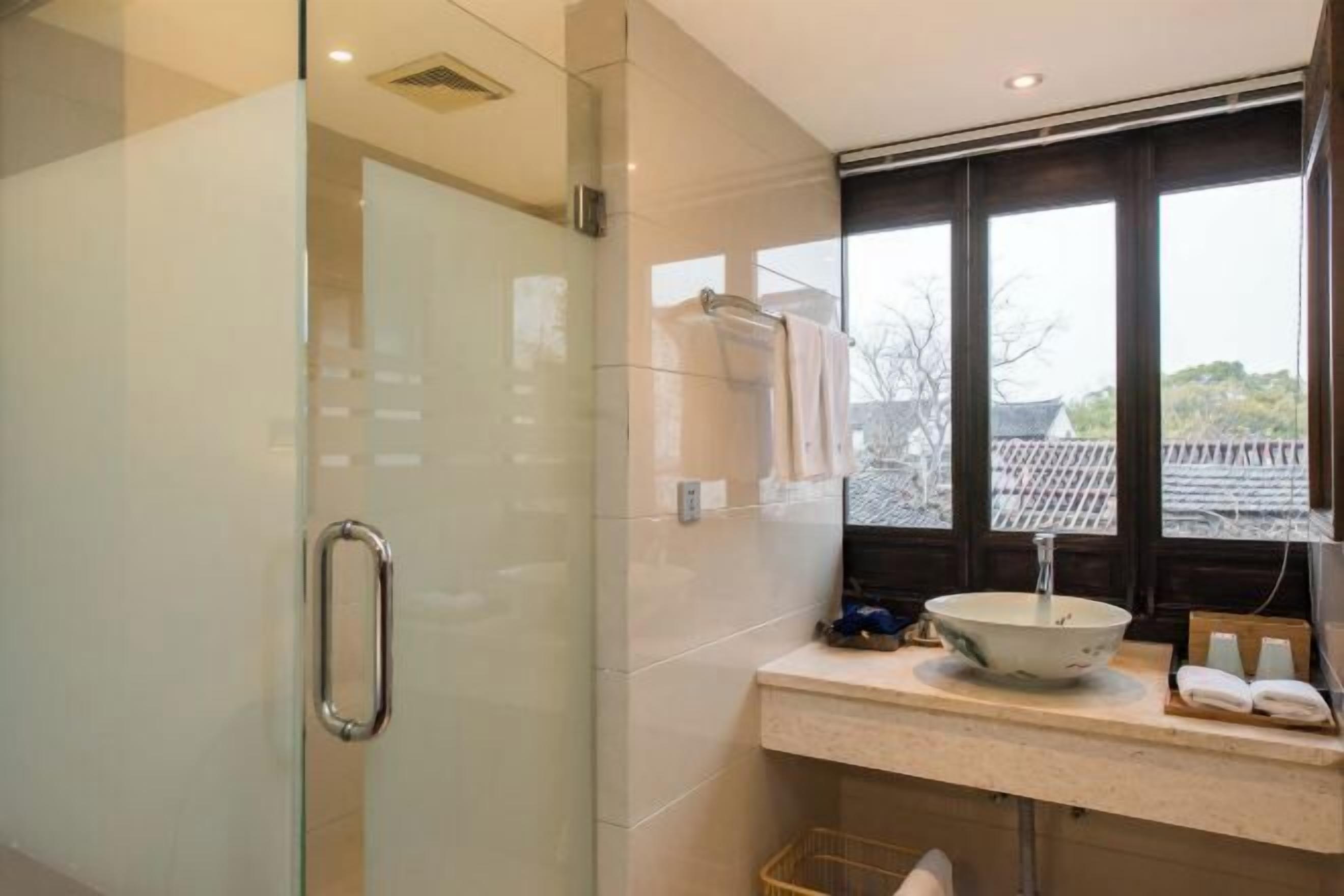 A modern bathroom with a glass shower enclosure, a sink with a bowl, and a window with a view of traditional architecture.
