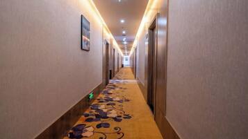 A hotel hallway with carpeted flooring, doors on both sides, and overhead lighting.
