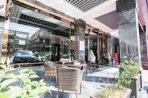 An outdoor seating area with wicker chairs and a table, a glass storefront, and a car parked outside. - Lanhao Boutique Hotel (Nantong)