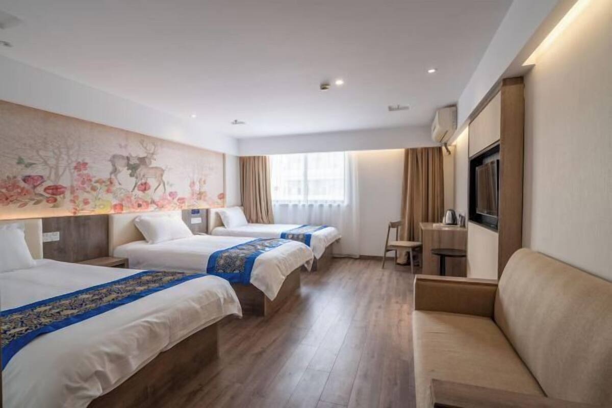 Ein Hotelzimmer mit drei Betten, einem Sofa, einem Fernseher und einem Wandgemälde.