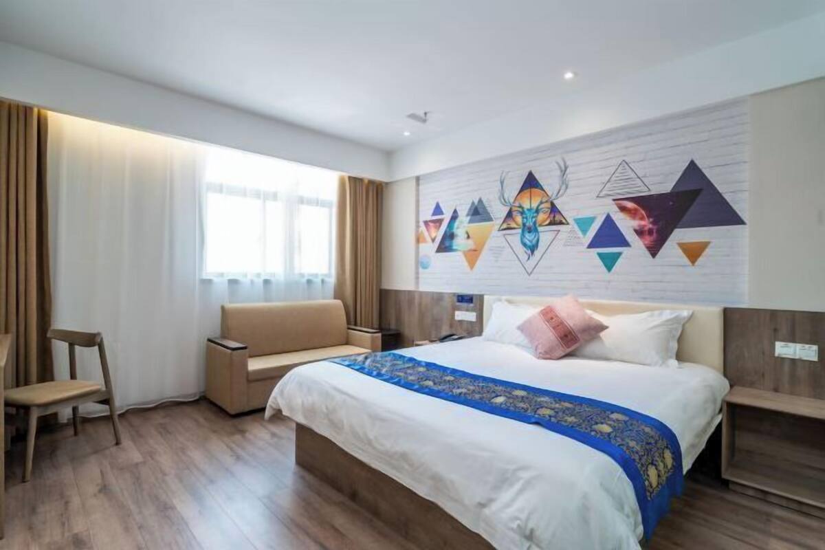Ein Hotelzimmer mit einem großen Bett, einem Sofa, einem Sessel und einer Wand mit geometrischer Kunst.