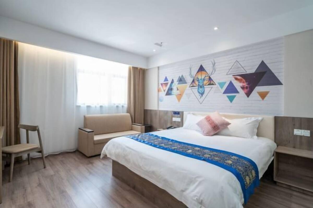 Ein modernes Hotelzimmer mit einem großen Bett, einer Couch, einem Sessel und einer Wand mit geometrischer Kunst.
