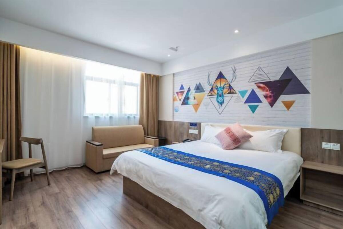 Ein Hotelzimmer mit einem Bett, einer Couch, einem Sessel und einer Wand mit geometrischer Kunst.