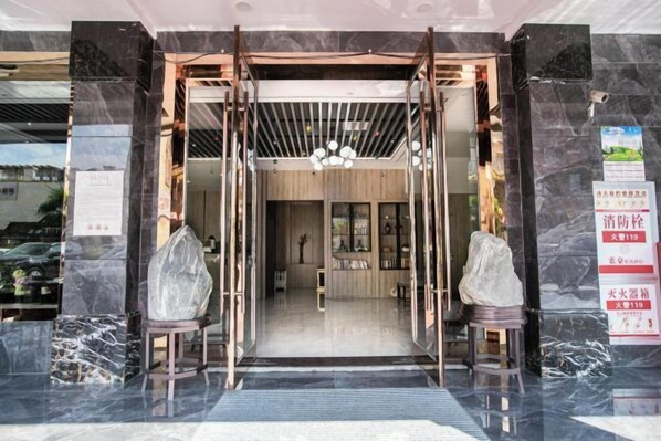 Entrada de hotel con puerta de vidrio, mostrador de recepción y vista del interior.